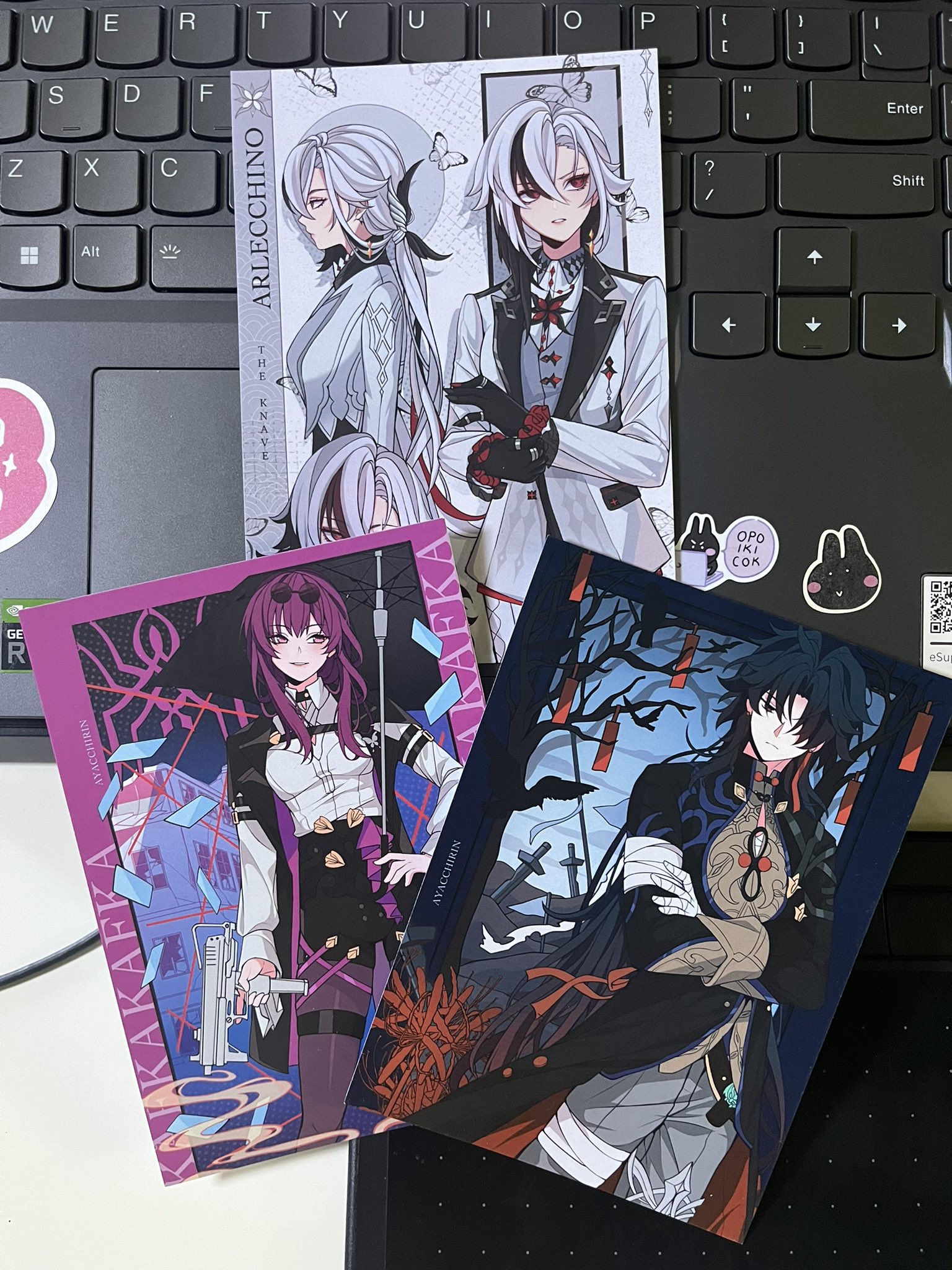 a close up image of three anime trading cards featuring characters from a popular japanese game. the cards are laid out on top of a laptop keyboard. the cards feature different characters with colorful backgrounds and artwork.