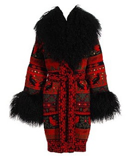 a long red and black knitted sweater with a black fur collar and black fur trim on the sleeves. the sweater has a red pattern with black and white details. the sweater is a long, wintery style. it appears to be made of wool.