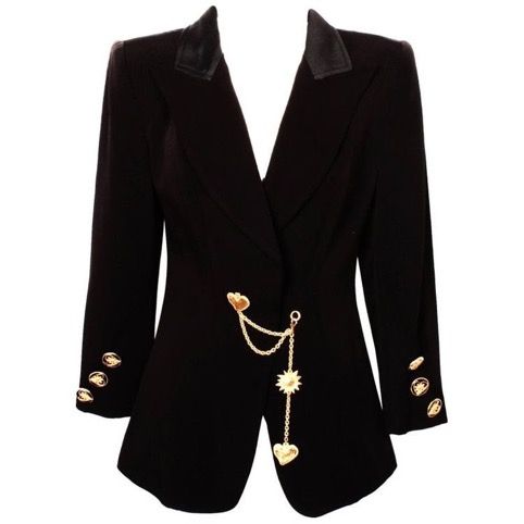 a black blazer with a gold chain hanging off the side. the blazer has a black lapel and gold buttons on the sleeves. the gold chain has a heart and sun charm.