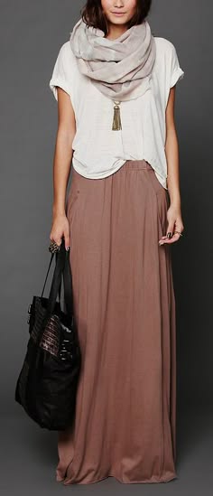 a woman wearing a white shirt, brown long skirt, and a scarf is posing for the camera. she has a black handbag slung over her shoulder. she is wearing a brown skirt and has a simple white top with a scarf.  the outfit is casual and simple, yet stylish.