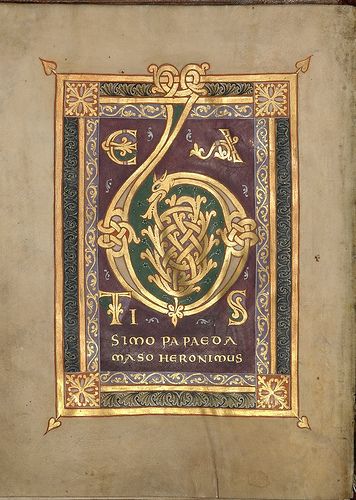 a closeup shot of an illuminated manuscript page featuring a large, elaborate capital "t" in gold and red against a purple background. the "t" is decorated with intricate knotwork and foliate patterns, and the surrounding frame is adorned with gold and red borders. the text surrounding the letter reads "simo paevae maso hieronymus,"  and the manuscript's design is characteristic of medieval artwork.