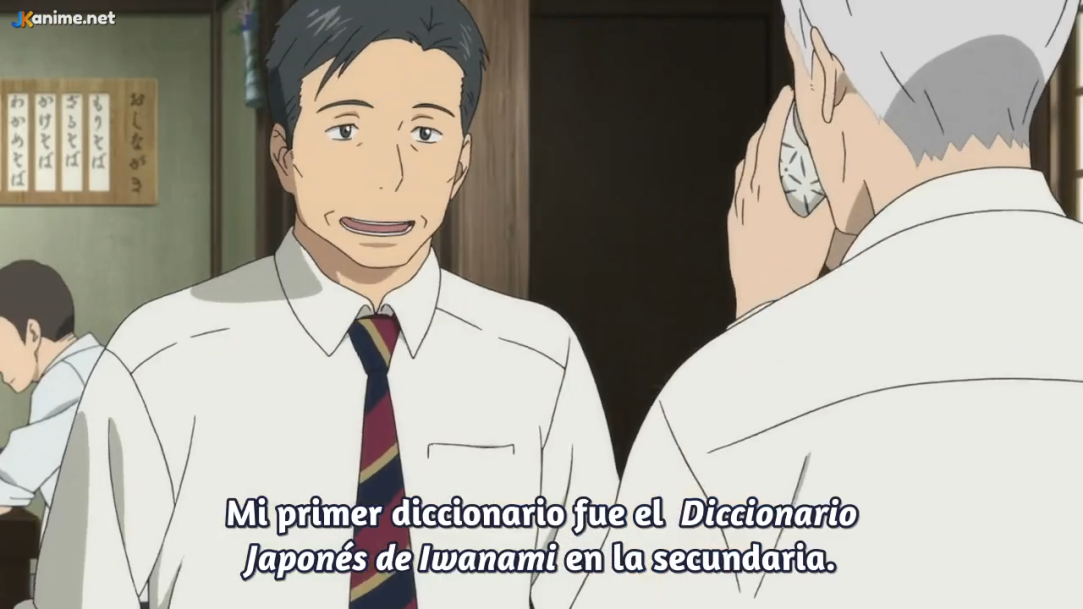two men are in a restaurant. the man on the left is wearing a white shirt and a striped tie. he is smiling and talking. the man on the right is wearing a white shirt and has gray hair. he is listening to the other man talk on the phone. the subtitles read, "mi primer diccionario fue el diccionario japonés de iwanami en la secundaria." which translates to "my first dictionary was the iwanami japanese dictionary in high school."```