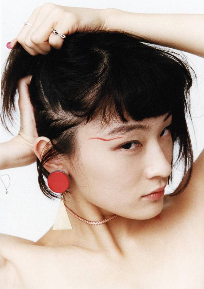 a young woman with black hair and bangs is wearing a red lipstick and red earrings and a white shirt. she is looking at the camera and has a casual style. she is wearing a choker and has a beautiful face.  her skin is clear and her eyes are bright.