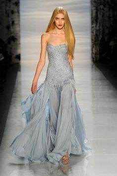 a blonde woman with long hair poses on a runway wearing a silver and blue strapless gown. the dress is long, flowing and has a train.  she is wearing silver shoes.