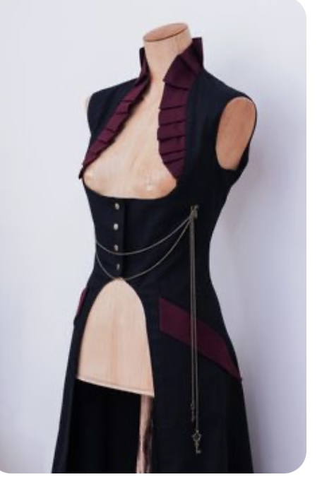 a formfitting, sleeveless steampunk dress in black is displayed on a mannequin. it has a deep vneckline with a burgundy ruffled trim, and a chain accent with a key dangling at the hem.