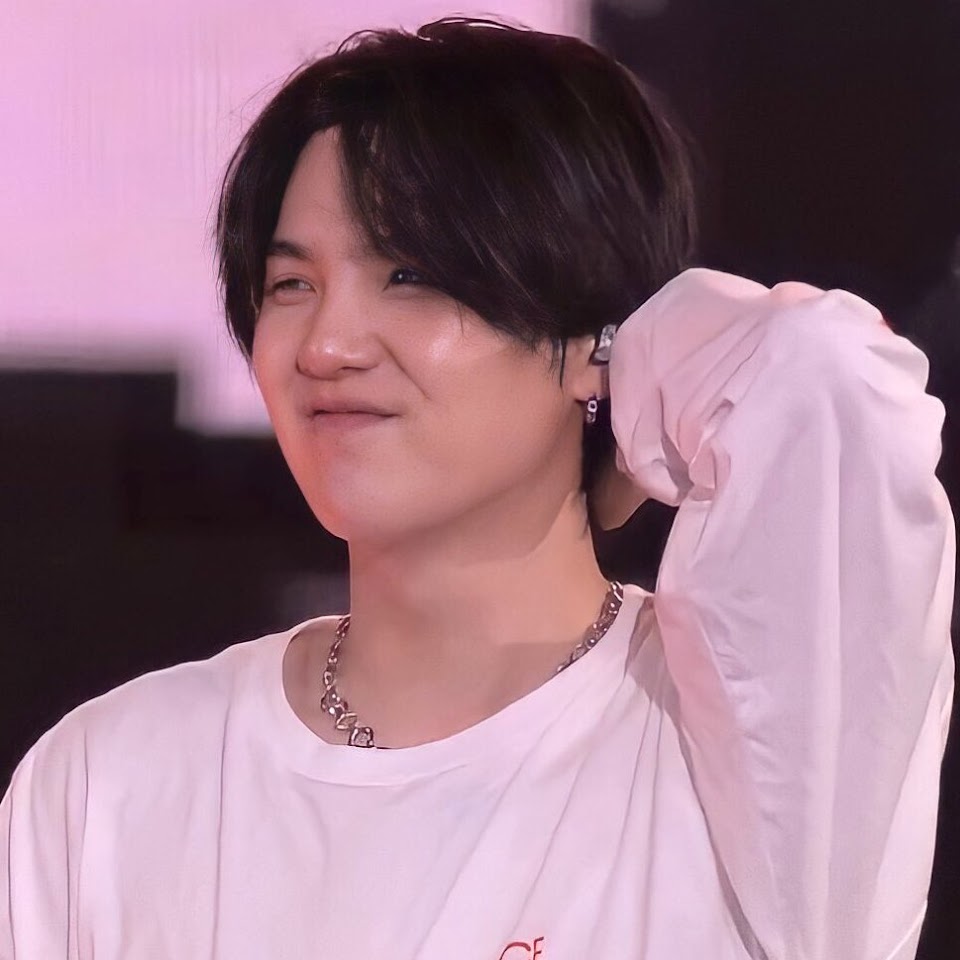 a portrait of min yoongi, also known as suga, of the kpop group bts. he is smiling slightly and has his hand raised near his head. he is wearing a white shirt and a silver chain necklace. he has black hair and an earring.