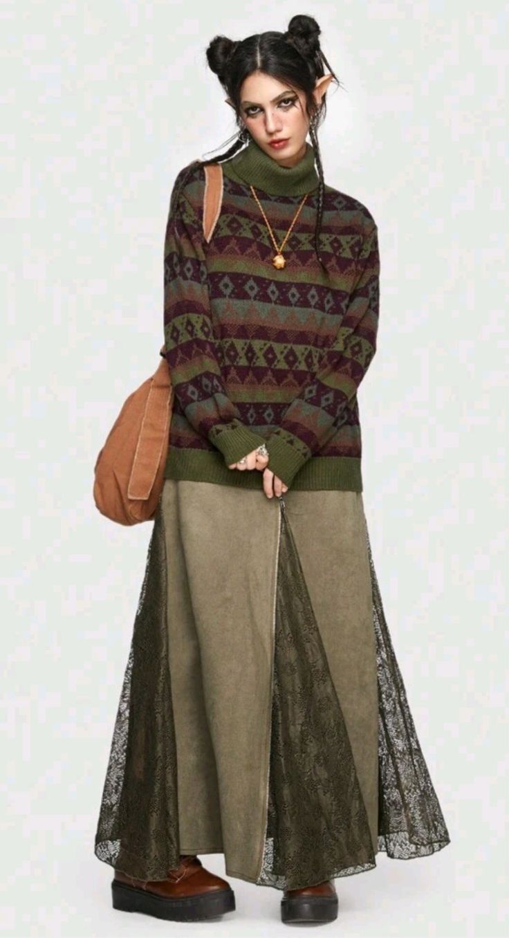 a fullbody shot of a woman modeling a fall/winter outfit. she's wearing a geometric patterned turtleneck sweater in shades of green, maroon, and brown. over it, she has a long, olive green skirt with a lace overlay. the skirt appears to be made of a heavier fabric, potentially corduroy or a similar material. her accessories include a brown crossbody bag slung over her shoulder and chunky brown boots. her hair is styled in two top knots and she sports small elflike ears. the overall style is reminiscent of bohemian or whimsical fashion. the background is a simple light neutral tone, ensuring the focus remains on the clothing and model.