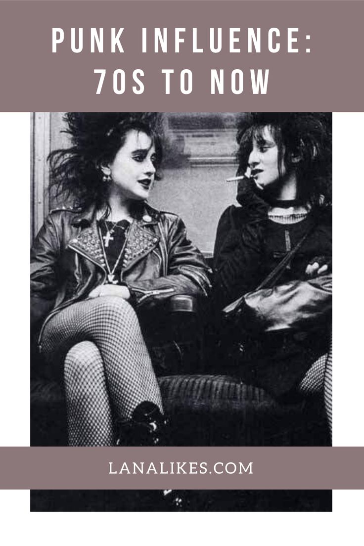 a black and white image titled "punk influence: 70s to now" showing two women in punk fashion sitting on what looks like a subway. the woman on the left is wearing a studded leather jacket, fishnet stockings, and a cross necklace. the woman on the right has short, dark hair and is holding a cigarette. the photo is taken in a public transport setting, likely a subway car. the overall aesthetic is associated with punk and goth subcultures.