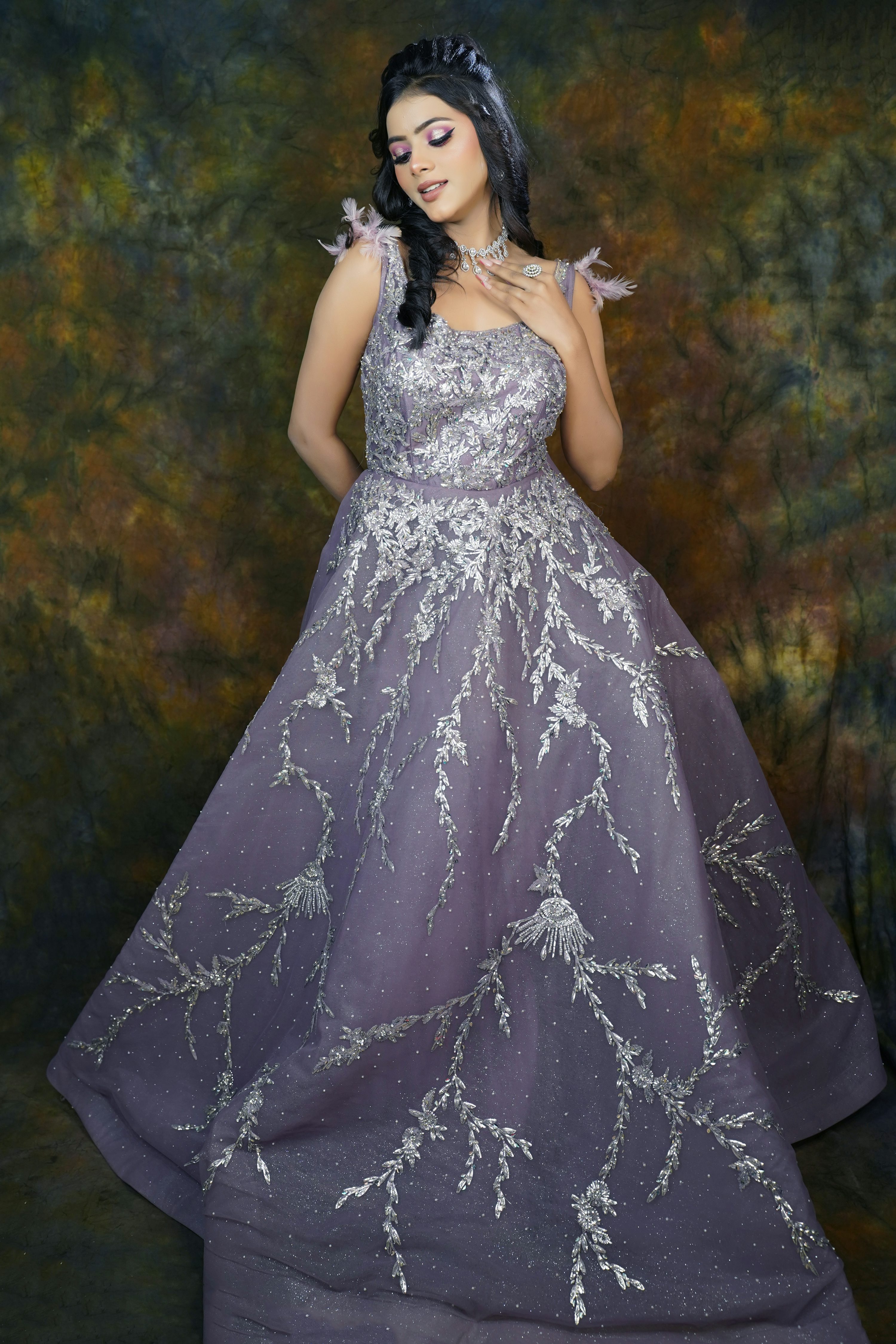 a captivating portrait of a woman elegantly dressed in a lavender gown. the dress features intricate silver embroidery throughout its tulle fabric, creating a stunning and detailed design. the gown is a floorlength ball gown, suitable for formal occasions like prom or a wedding. the woman's makeup is flawless and her dark hair is styled in an updo. she's adorned with delicate jewelry. the backdrop is a muted, textured background that subtly enhances the beauty of the dress and the model. the overall mood of the image is sophisticated, graceful, and timeless.