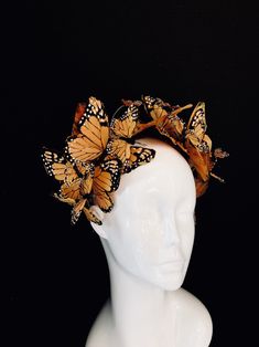a white mannequin head is adorned with a stunning handcrafted butterfly crown. the crown features realisticlooking monarch butterflies in various shades of orange and brown, arranged in a circular pattern. the intricate details and lifelike appearance of the butterflies create a striking and elegant statement piece.