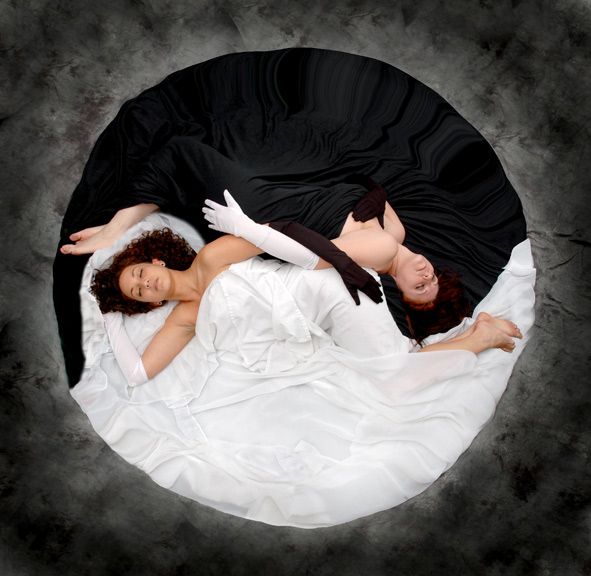 two women are laying on a circular surface, each in a contrasting color  one dressed in white and the other in black. they are embracing, their bodies intertwined in a pose that represents the yin yang symbol. the white woman is on the right side, and the black woman is on the left side. the image symbolizes the balance and harmony between opposites.