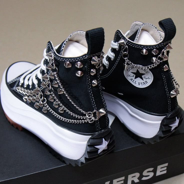 a pair of black and white converse chuck taylor all star high top sneakers with chunky platform soles. the shoes are adorned with silver chains and spikes.  they are shown on a black surface with a white converse label visible.