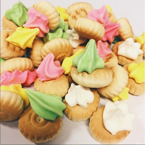 a closeup shot of a variety of colorful cookies with different frosting. the cookies are small and round, and they are arranged in a pile on a white surface. the frosting is in various colors, including pink, green, yellow, and white. there are also some sprinkles on the cookies.