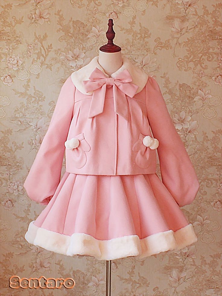 a pink lolita fashion dress set consisting of a jacket and a skirt is shown on a mannequin against a floral background. the jacket has a peter pan collar, a large bow at the collar, two pompoms on the front, and puffed sleeves. the skirt is short and flared, with a band of white faux fur at the hem.