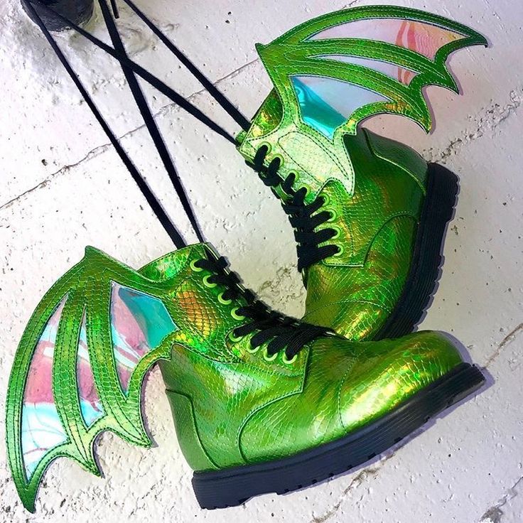 a pair of green, iridescent ankle boots with black laces and dragon wings attached to the back are displayed on a white surface. the boots feature a snakeskin texture. the wings are iridescent and have a unique shape.