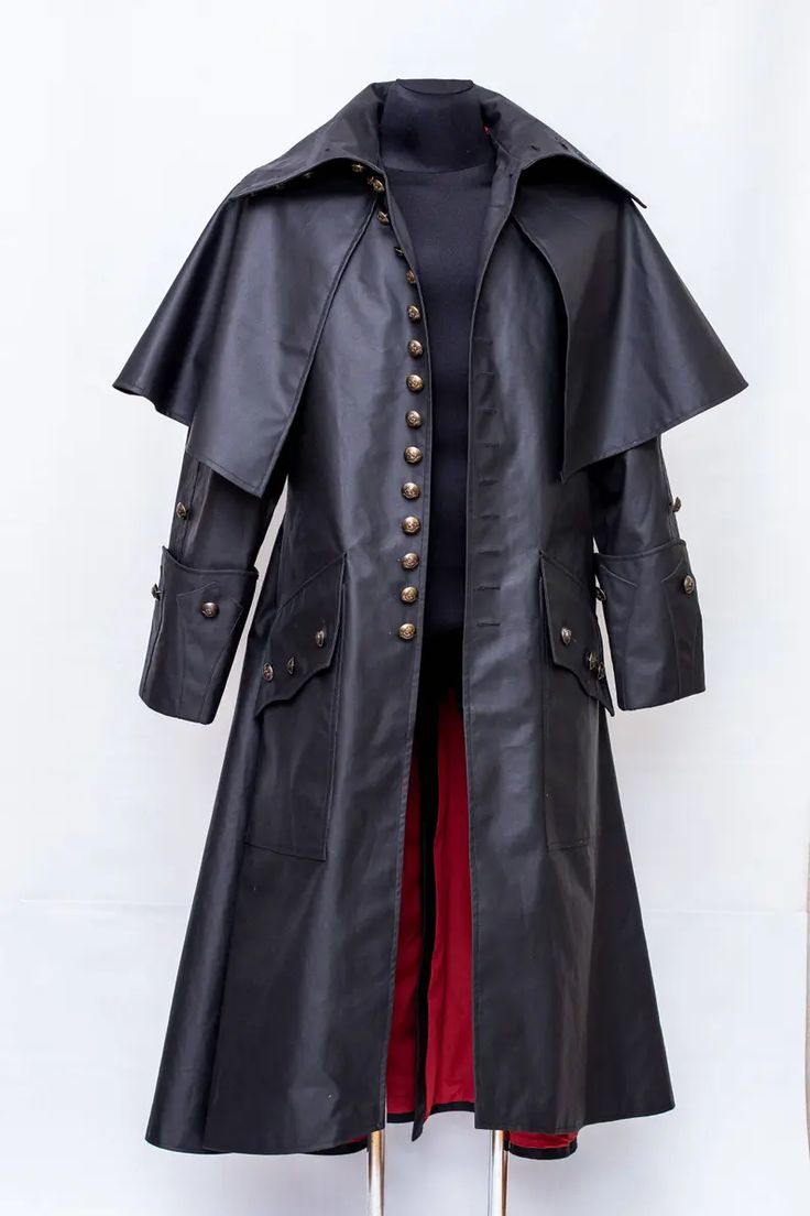 a black, leatherlike coat with a cape attached. it is long, going down to the midcalf area. the coat has brasscolored buttons down the front and on the sleeves. there are also flap pockets on both sides. the inside of the coat is lined with red fabric. it is displayed on a mannequin against a white background.