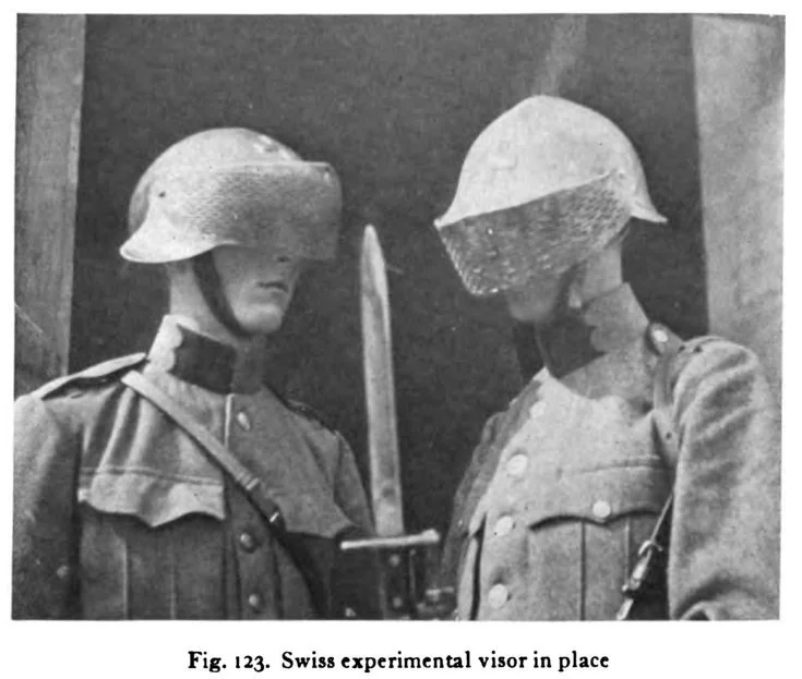 two swiss soldiers stand facing each other. the soldier on the left wears a traditional swiss helmet with a metal visor in place, while the soldier on the right wears a similar helmet, but with a different visor. the soldier on the left has a bayonet attached to his rifle.