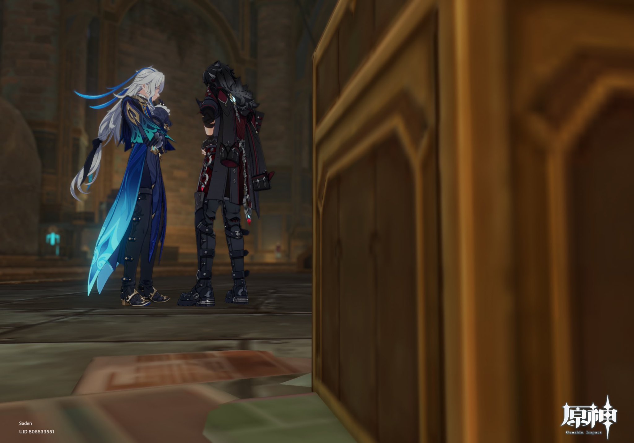 screenshot from the video game genshin impact shows two male characters standing in a dimly lit stone room.  one character has long white hair and a blue and black outfit, while the other has dark hair and wears dark clothing. they appear to be in conversation. a large, ornate wooden chest is partially visible in the foreground. the overall style is animeinspired fantasy. the genshin impact logo is visible in the bottom right corner.