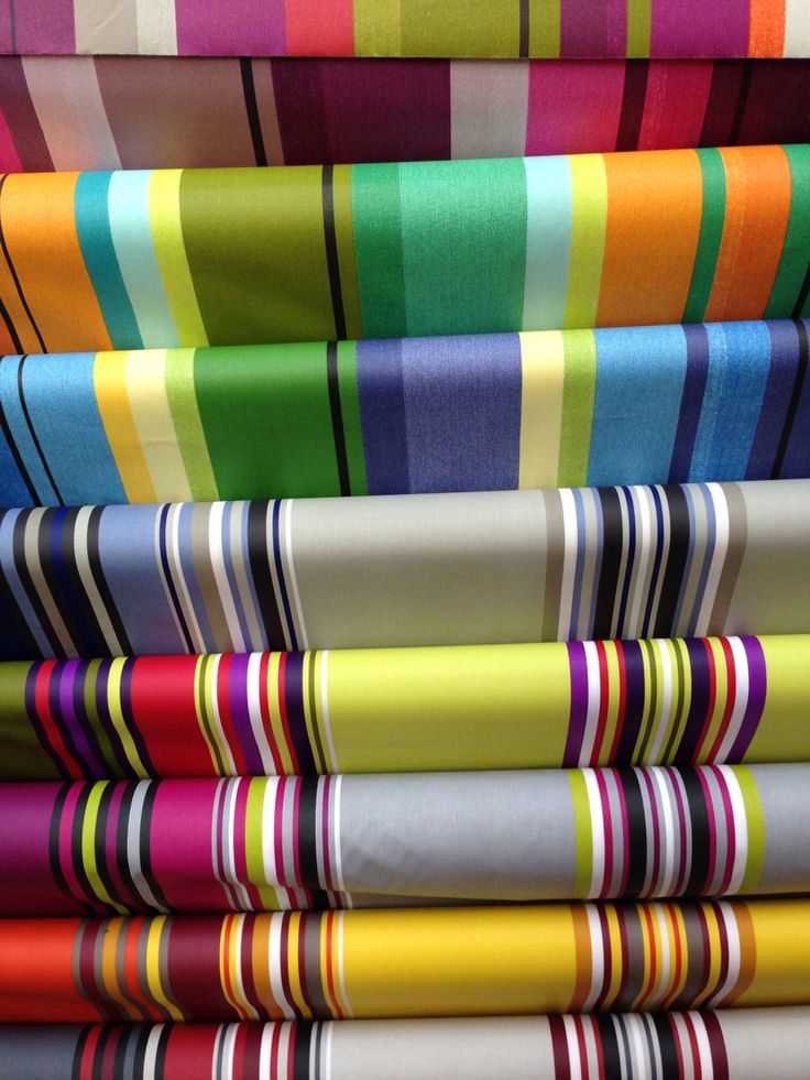 a stack of different brightly colored striped fabrics. the fabrics are all woven with a variety of colors and patterns. the top fabric is a light pink and white stripe, and the bottom fabric is a dark blue and white stripe.
