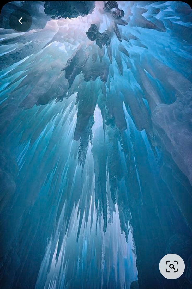 the image captures the interior of an ice cave, showcasing a multitude of icicles hanging from the ceiling. the ice exhibits a blue hue, indicating its density and purity. the scene is illuminated by an ethereal light that filters through the ice.