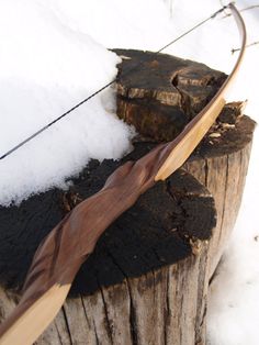 a handcrafted wooden bow and arrow rests on a snowcovered tree stump. the bow's intricate carvings are highlighted against the white snow and dark wood, showcasing the craftsmanship. the snowy environment suggests a winter setting, adding to the rustic and natural feel of the image.