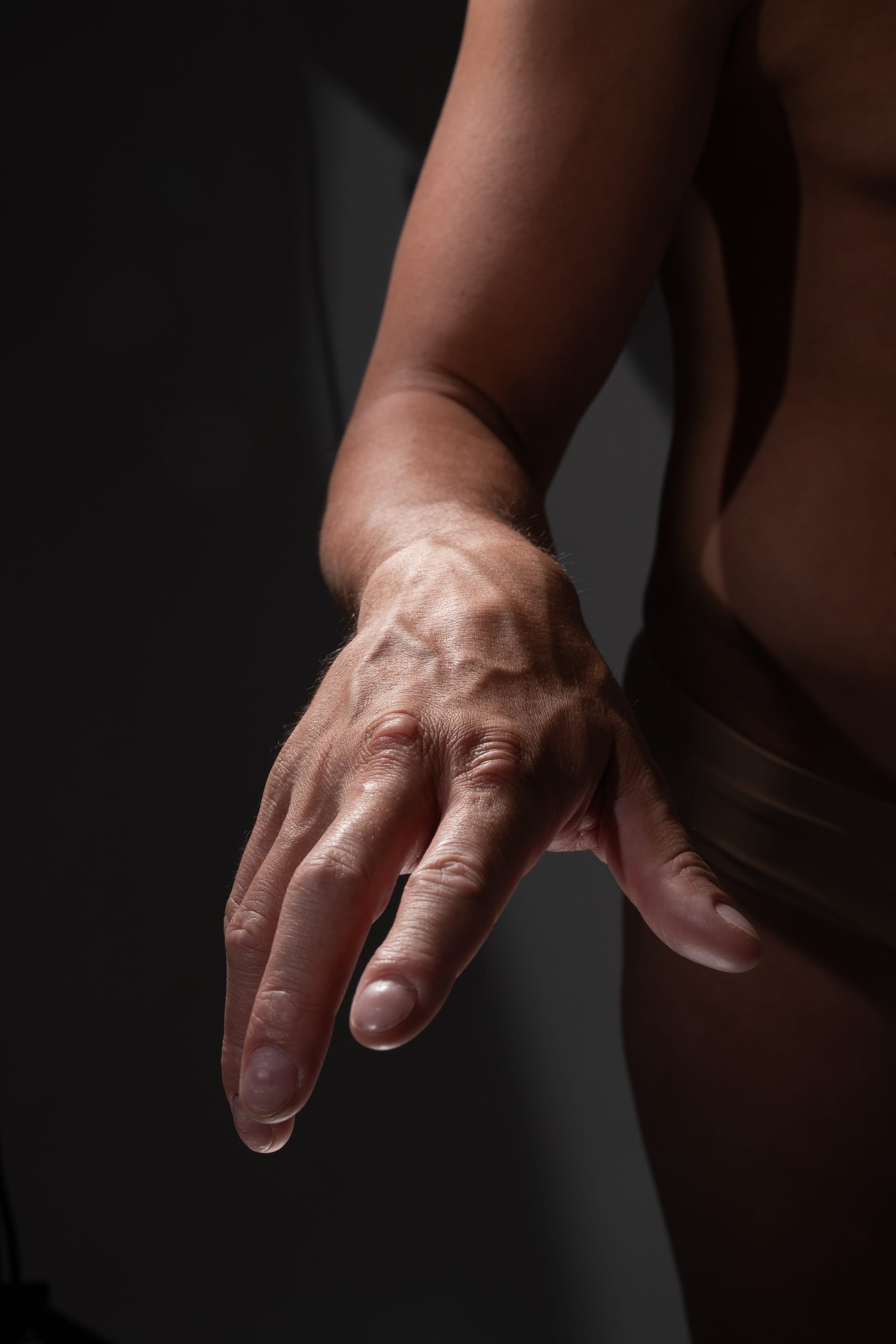 a closeup shot of a person's outstretched arm and hand illuminated by natural light.  the arm is extended with fingers spread, showcasing the details of skin texture and veins. the lowkey lighting casts deep shadows, creating a dramatic contrast.
