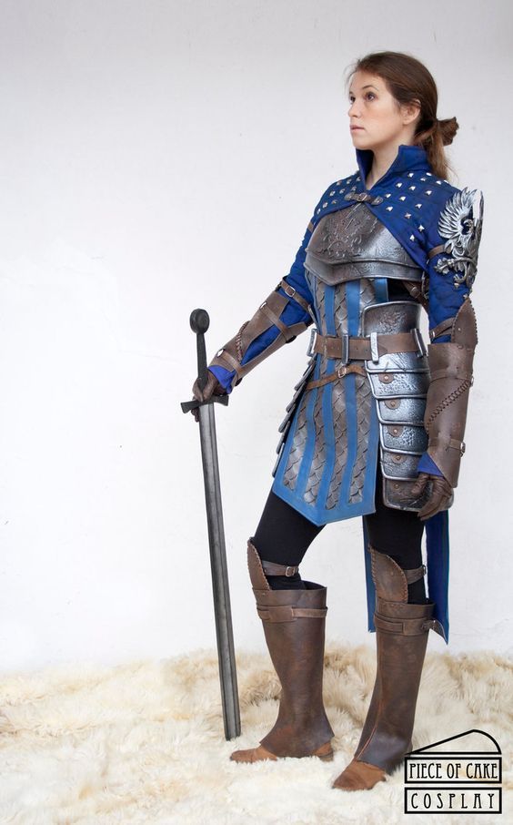 the image showcases a highquality ciri cosplay from the witcher 3: wild hunt. the cosplayer is a woman, posing with a long sword. she's wearing a meticulously crafted costume, replicating ciri's signature blue and silver armor with remarkable detail. the armor includes leather components and appears intricately designed. her boots are long and brown, matching the style depicted in the game. the setting is a simple, clean studio background with a white fur rug.  the image is professionally taken, focusing on the detail and accuracy of the cosplay. a watermark "piece of cake cosplay" is visible in the bottom right corner.