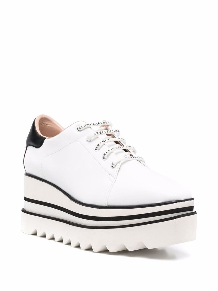 he image shows a pair of stella mccartney women's white platform sneakers. the shoes are laceup and feature a thick platform sole with a scalloped edge. the laces have the stella mccartney logo printed on them. the shoes appear to be made of leather or a similar material. the background is plain white, allowing the shoes to stand out. the shoes are stylish and seem suitable for spring and summer wear.