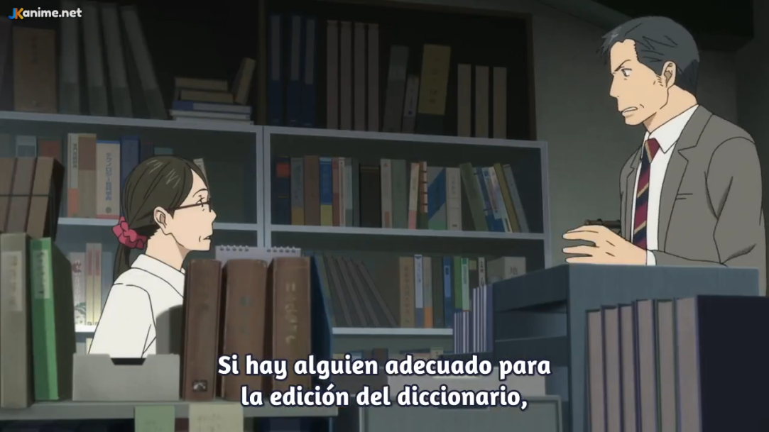 in an office or library setting, a man and a woman are engaged in a conversation. the man, dressed in a suit, stands by a desk with bookshelves behind him. the woman, wearing glasses and a white shirt, sits at the desk. the lighting suggests an indoor setting, and the overall color palette is muted and realistic, typical of anime. the perspective is from eye level, placing the viewer in the position of an observer. the image captures a moment of dialogue, possibly related to the editing of a dictionary, as indicated by the text at the bottom of the image.