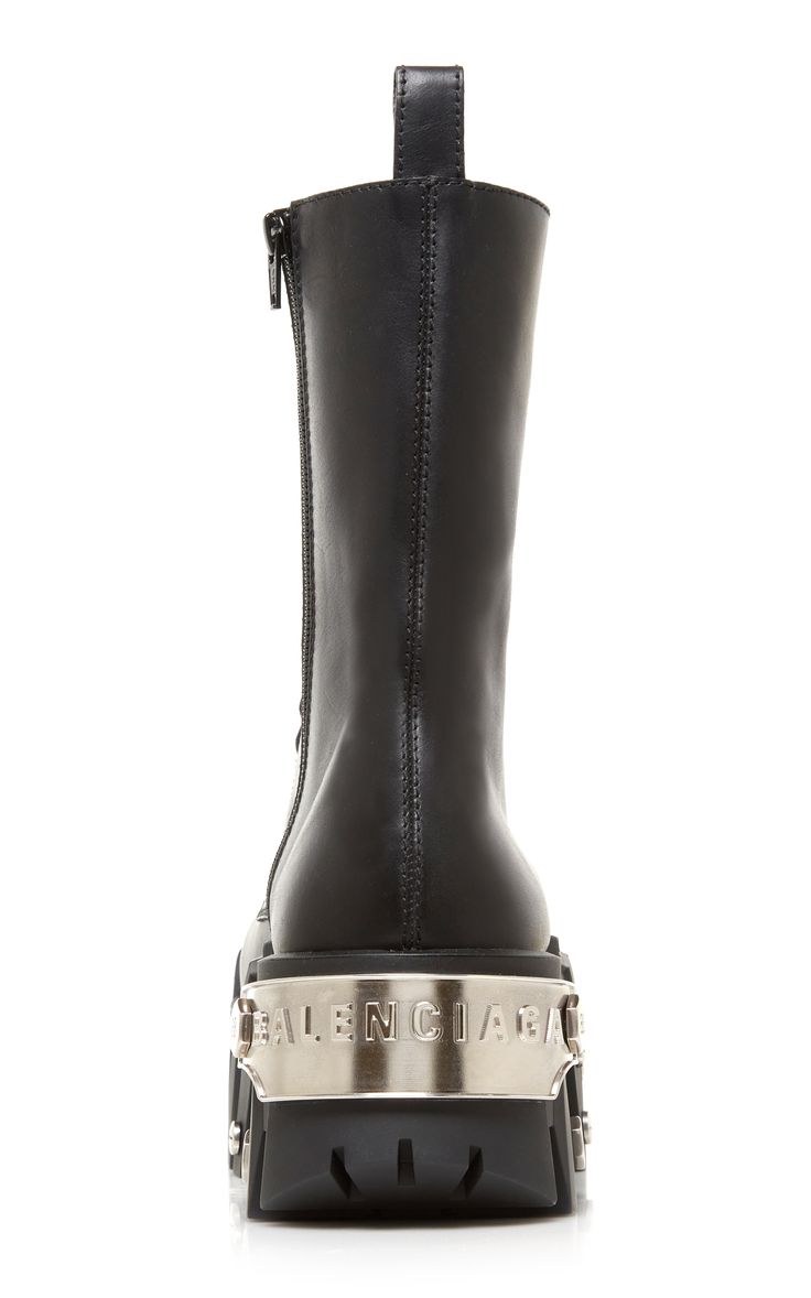 a pair of black leather balenciaga platform boots is shown.  the boots are high, have a chunky platform sole, and feature the balenciaga logo embossed on a silver metal band around the sole.  they zip up the side.  the image shows the boots from the side, set against a white background.