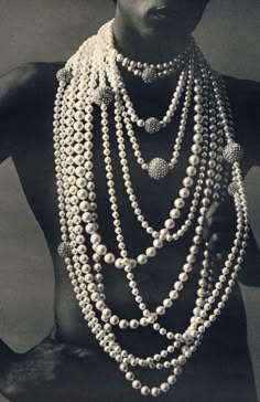 a black and white portrait of a woman wearing a multiple strand pearl necklace that drapes down her chest. the woman is posed against a dark backdrop, with only her face and shoulders visible. the image is a classic representation of beauty and elegance.