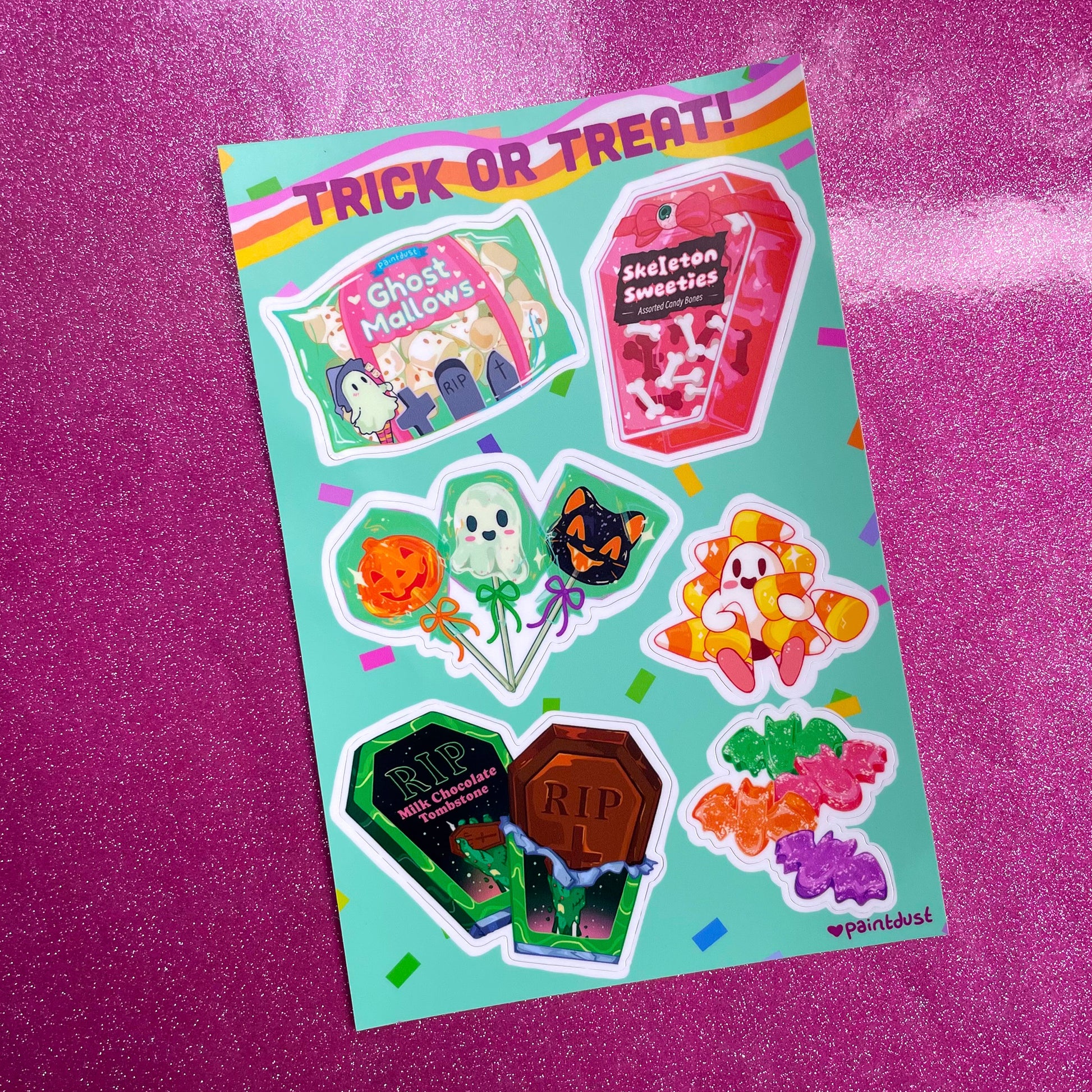 a closeup shot of a vibrant sticker sheet featuring various cute halloweenthemed treats.  the sheet is teal and features illustrations of ghost marshmallows, skeleton sweets in a coffinshaped box, lollipop ghosts and pumpkins, candy corn, batshaped candies, and milk chocolate tombstones. the top of the sheet reads "trick or treat!" in a playful font. the stickers are in a kawaii style and are brightly colored. the sheet is placed on a sparkly pink background. the bottom right corner shows the artist's signature: paintdust.