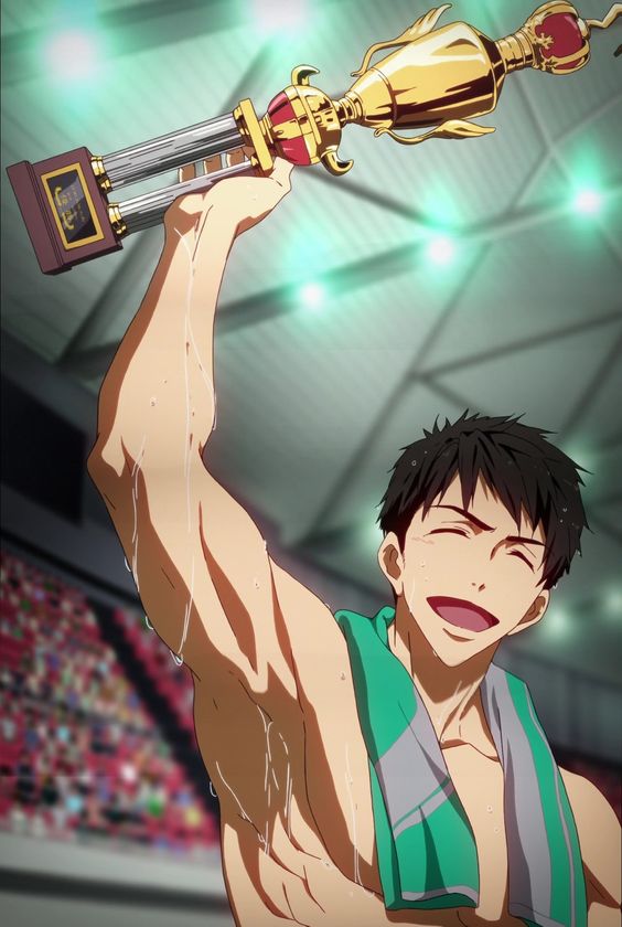 a young, muscular man with short dark hair and a bright smile holds a large gold trophy above his head. water drips from his body and the trophy, indicating he was recently in a pool. he has a green towel around his neck. the background is out of focus, but a crowd of people and stadium lights are visible, suggesting he is celebrating a victory after a competition.