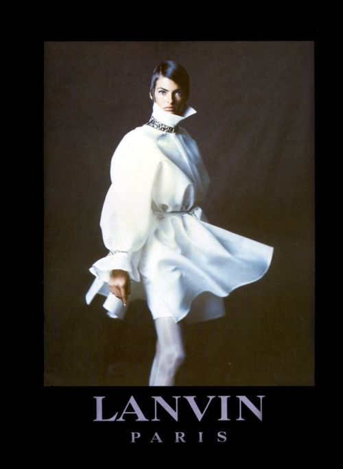 this is an advertisement for lanvin paris. it features a woman modeling a white dress with a collar and belt on a black background.