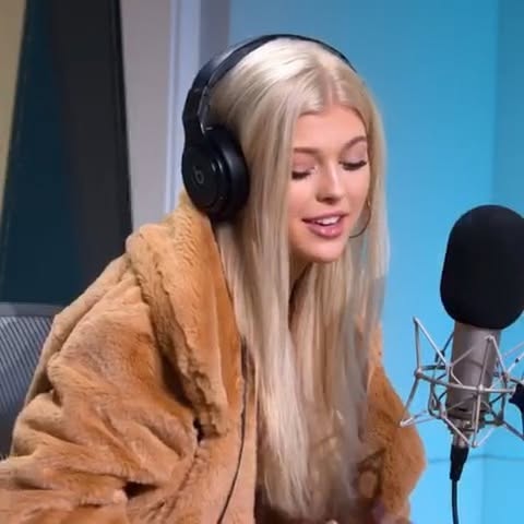a woman with blonde hair wearing a fur coat and headphones is sitting in front of a microphone in a recording studio.