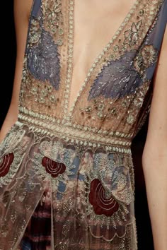 a closeup of a woman wearing a beautiful, intricately beaded and embroidered dress. the dress is sheer and lace, with a deep vneckline. the beading is intricate and detailed, and the lace is delicate and feminine. the dress is a stunning example of couture fashion.