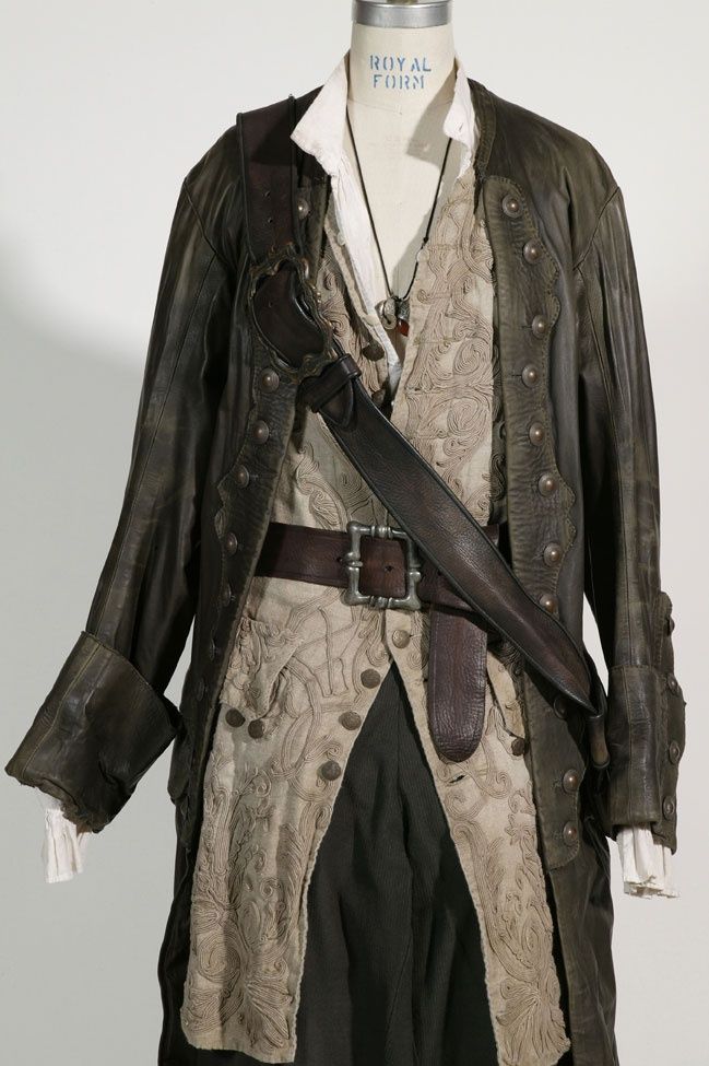 a mannequin is dressed in a detailed pirate costume, featuring a weathered dark jacket, an ornate offwhite vest with decorative patterns, a white collared shirt underneath, and a dark sword sheath and belt. a necklace hangs around the mannequin's neck. the costume is displayed against a plain white background.