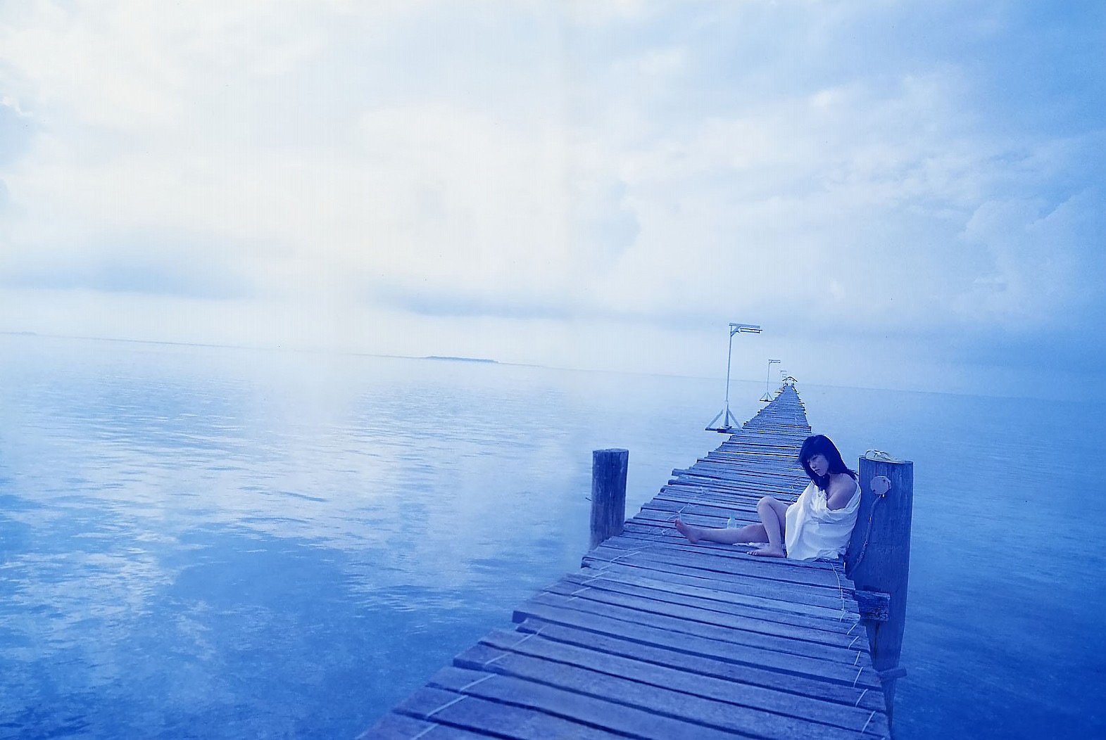 a young woman in a white dress sits on a weathered wooden dock that extends into a serene blue ocean. the vastness of the sea and sky, painted in soft shades of blue, create an atmosphere of tranquility and solitude. the woman appears lost in thought, perhaps contemplating the endless horizon.