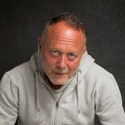 a closeup portrait of a middleaged caucasian man with grey hair and a beard wearing a grey hooded sweatshirt looking directly at the camera with a serious expression. the background is black.