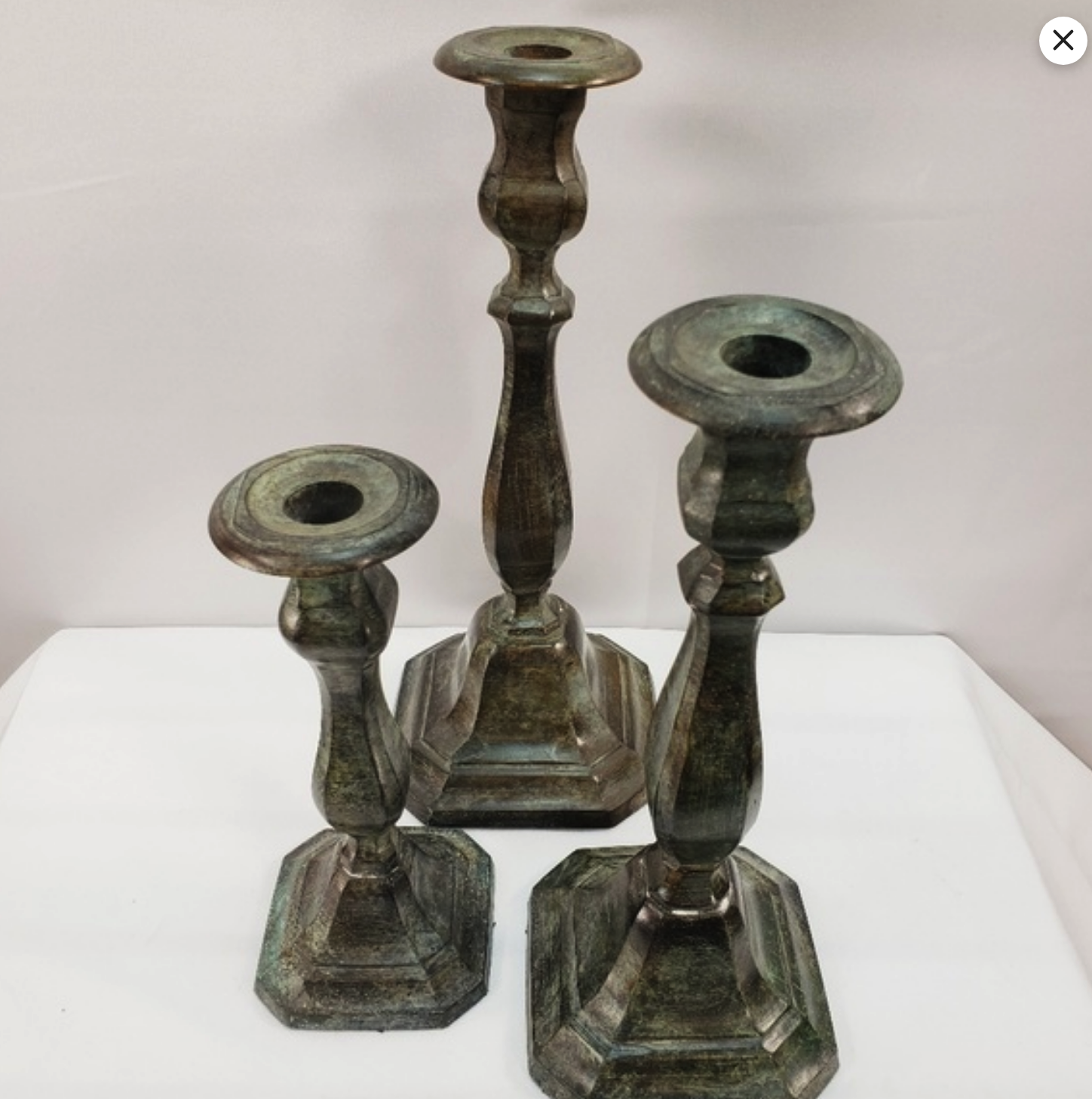 three ornate metal candle holders on a white background. the candlesticks are all different sizes and shapes, and they have an antique look. the tall candle holder in the middle is silver and has a round base. the two candle holders on either side of the tall one are both bronze and have a square base. they're all arranged in a symmetrical way and would make a great centerpiece for a wedding or party.