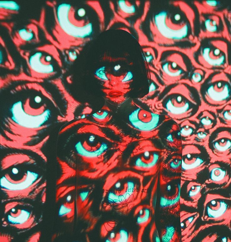 the image showcases a woman with a short, dark bob haircut standing against a background entirely covered in a projected pattern of numerous large eyes in shades of red and teal. the projection appears to overlay her body, creating a surreal and psychedelic effect where the eyes seem to be painted onto her skin. the overall atmosphere is mysterious, intense, and artistic, combining fashion and visual art in a unique and creative way.  the contrast of the red and teal is striking and the repetitive eye motif is captivating.