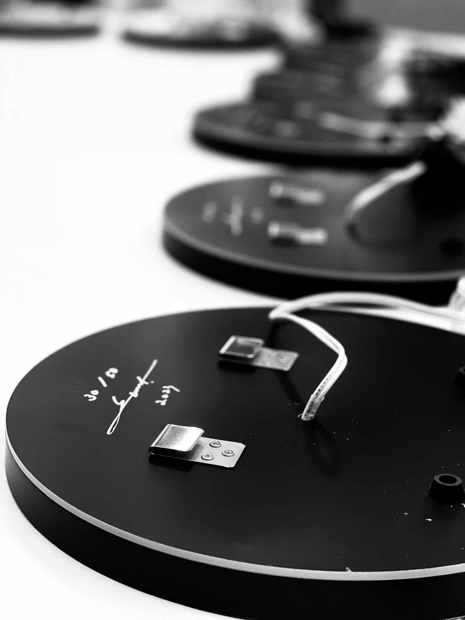the image shows a closeup view of a series of circular electronic devices, likely led lights or similar, laid out in a row. the devices have a black and white color scheme, with the majority of their surface being black and a thin white border. visible details include wires, metallic components, and markings on the underside. the shallow depth of field emphasizes the texture and pattern created by the arrangement of the devices, highlighting their circular shape and the repetition within the image. the overall impression is one of modern technology and minimalist design.