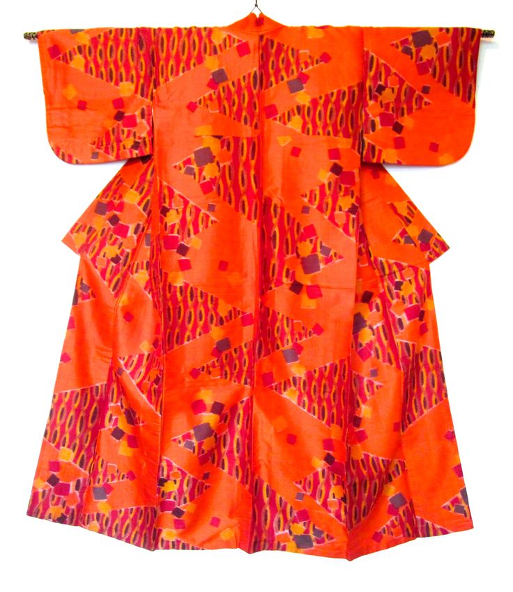 an orange kimono with geometric patterns hanging on a hanger. the kimono has a triangle design with overlapping ovals and scattered squares in shades of red, orange, yellow, and purple.