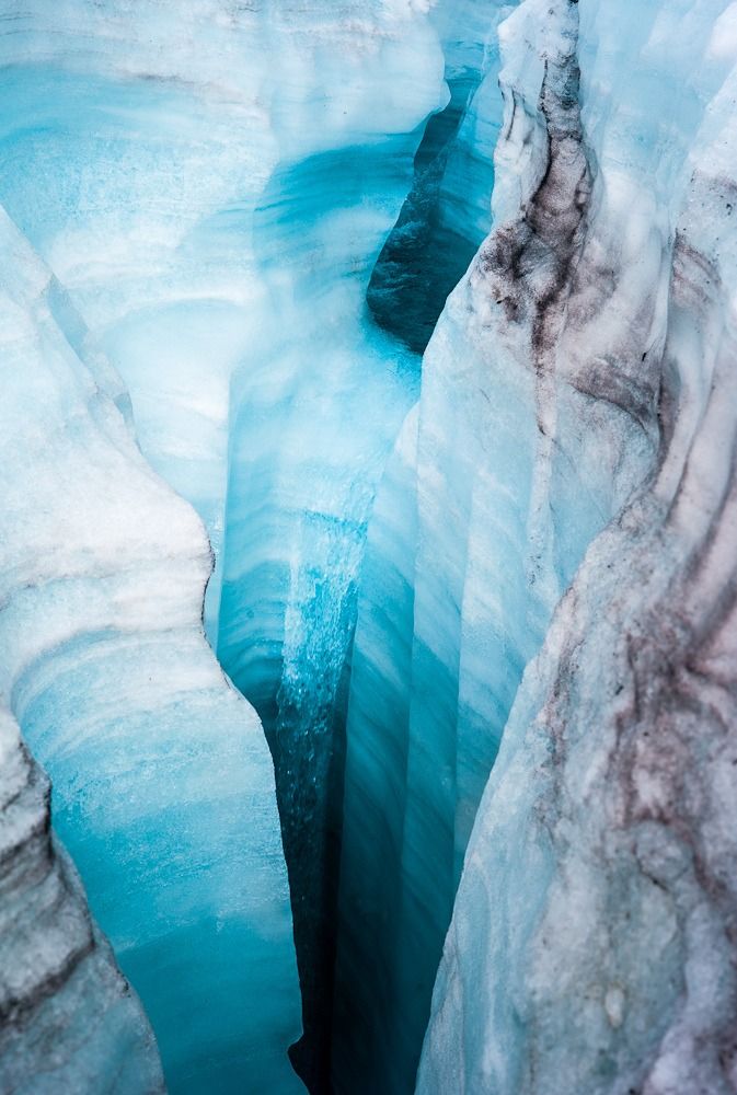 a closeup view into a deep crevasse in a glacier, showcasing the vibrant blue ice and its unique texture. the shot emphasizes the depth and coldness of the environment.