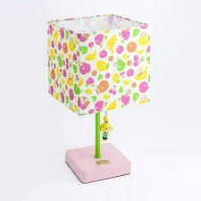 a colorful lamp featuring a square lampshade adorned with a fruity pattern that includes bananas, apples, and cherries. the lampshade is topped with a white background. the base is a light pink square, and a bright green pole connects the base to the lampshade. a small isabelle from animal crossing charm hangs from the pole, adding a playful touch. the lamp is set against a plain white background.