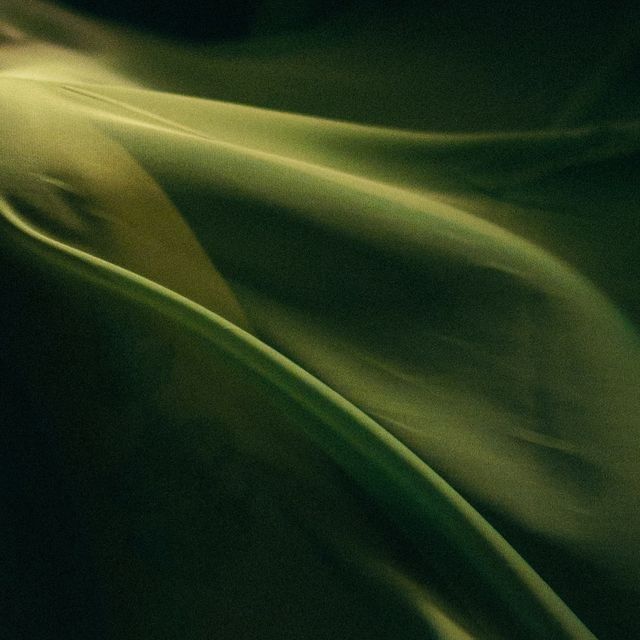 a closeup abstract image of dark green fabric, flowing and rippling in a soft, smooth and elegant manner. the fabric creates a sense of depth and movement. the background is dark and blurry. the image has a minimal and simple design, with a focus on the texture of the fabric.
