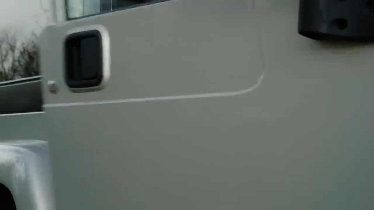 the image shows a closeup view of a silver car door. the door is closed, and the handle is visible. the car appears to be parked outside on an overcast day.