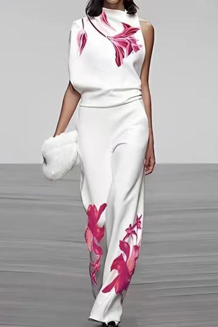 a woman in a white floral print pant suit with her arm crossed. she's walking on a runway during a fashion show.