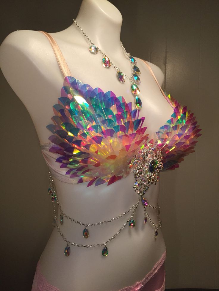 the image features a white mannequin wearing a decorative iridescent bra, a necklace, and a belly chain. the bra is adorned with shiny sequins, giving it a colorful and reflective appearance. a jeweled piece is attached between the bra cups. the necklace, draped around the mannequin's neck, is made up of clear stones. a silvercolored belly chain with teardropshaped pendants hangs from the bra and around the mannequin's waist. the mannequin is positioned against a neutralcolored background.