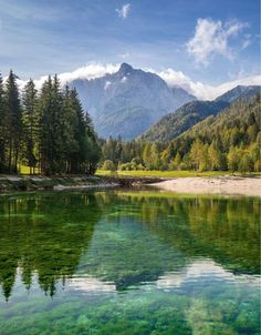 the image showcases a breathtaking alpine landscape. a serene lake with crystalclear turquoise water mirrors the majestic mountain range towering in the background. lush green trees and vegetation frame the lake, creating a vibrant and tranquil scene. the sky is a brilliant blue with fluffy white clouds, adding to the picturesque beauty of the landscape.
